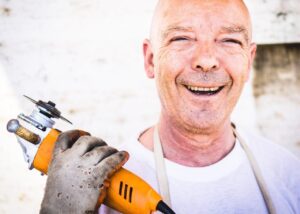 Man smiling holding a hand tool.