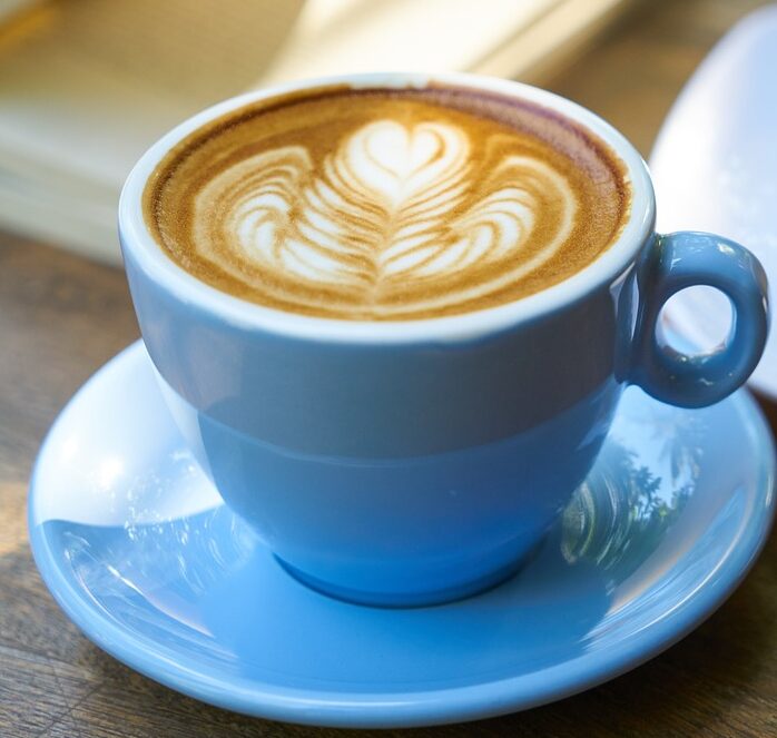 Blue cup of coffee next to a slice of cake.