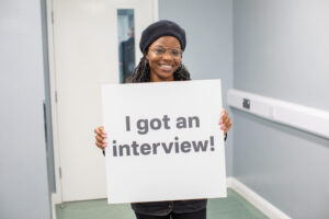 Woman smiling and holding sign saying 'I got an interview.'