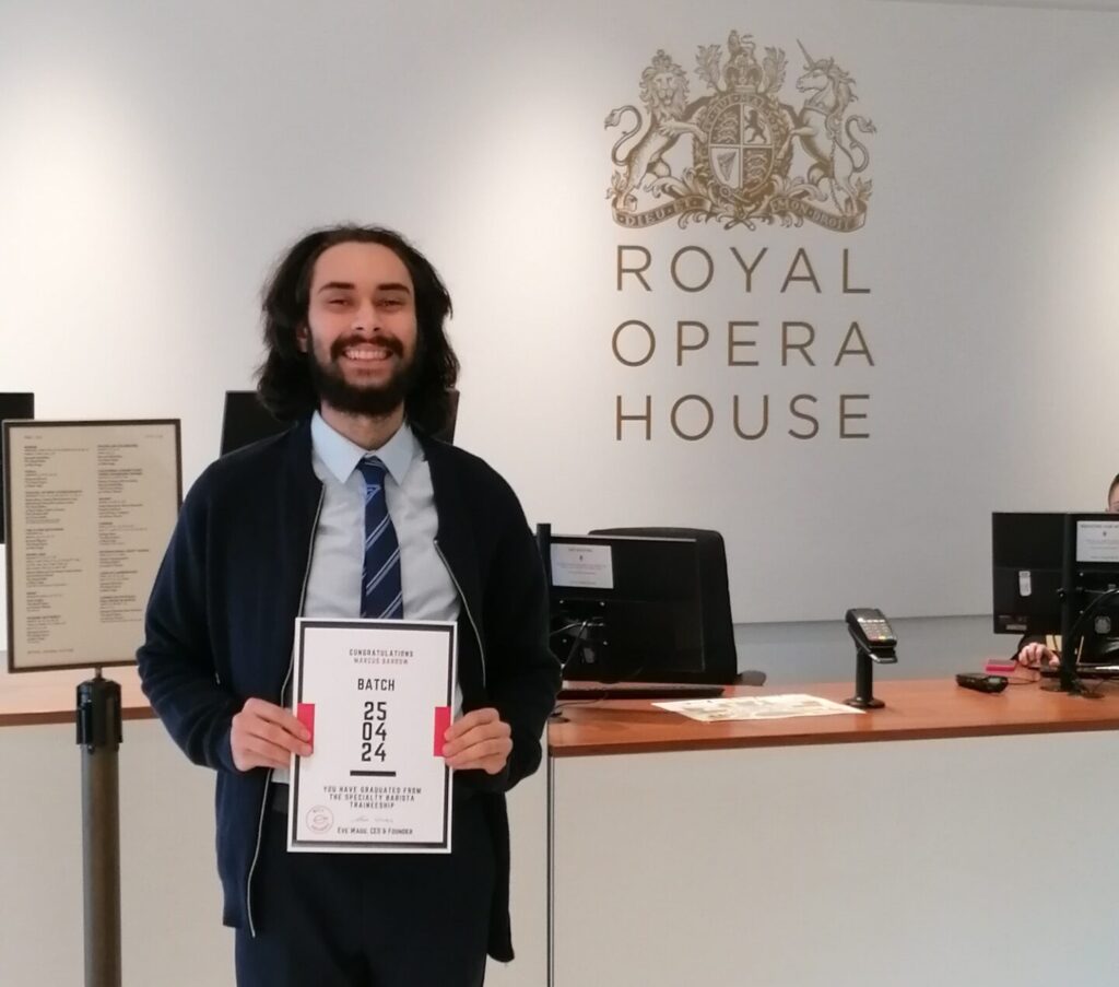 Photo of Marcus holding a certificate in front in the reception of the Royal Opera House